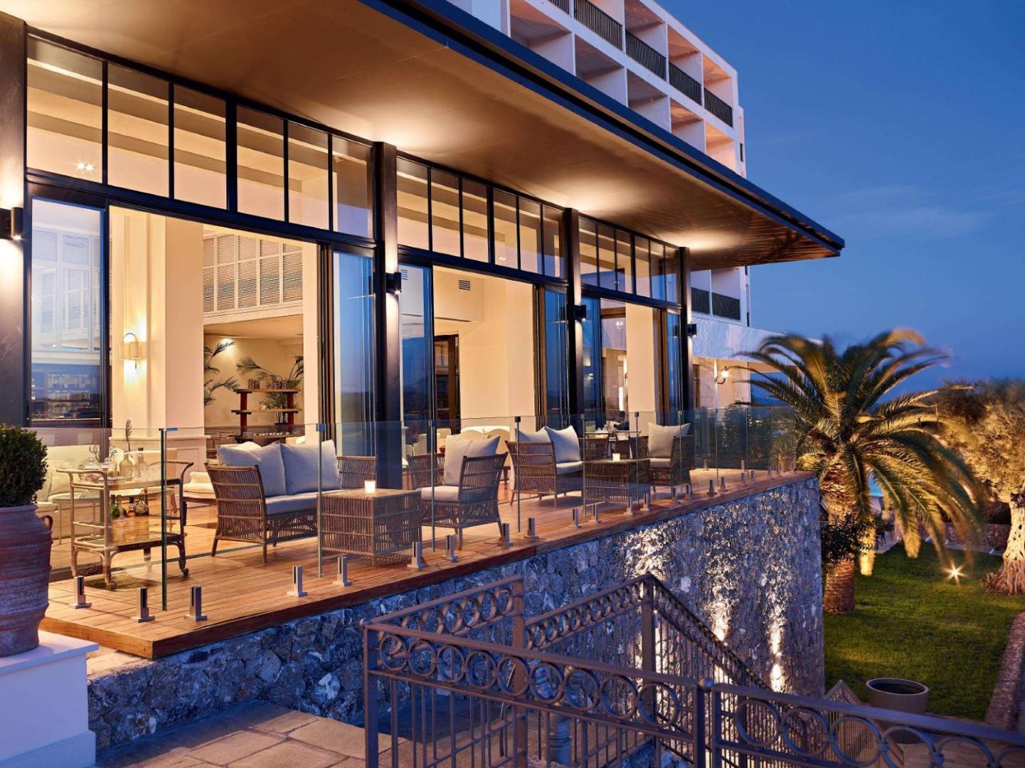 Corfu Imperial Grecotel Exclusive Resort vakara apgaismojums uz terases ar ērtiem krēsliem un skatu uz dārzu