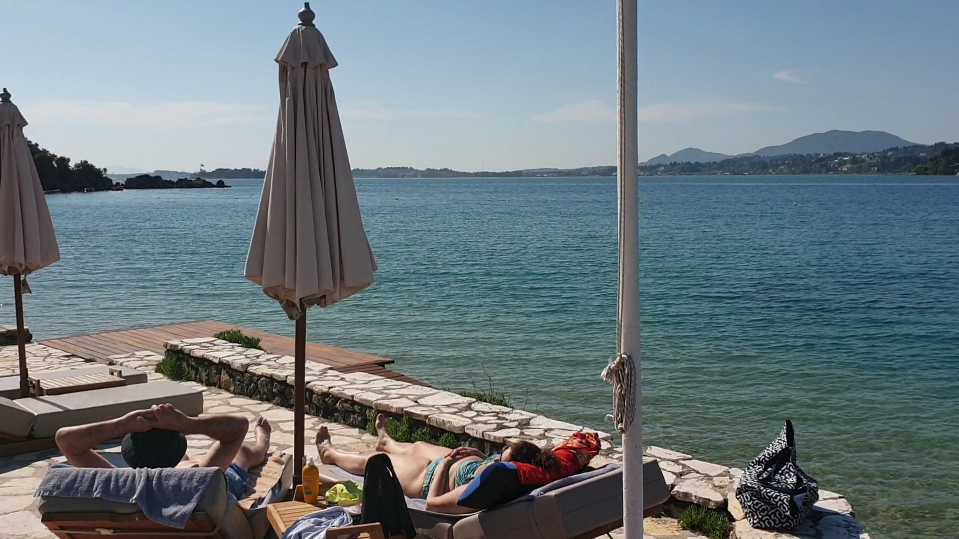 Viesi atpūšas Corfu Imperial Grecotel Exclusive Resort pludmales zonā uz sauļošanās krēsliem pie pašas jūras malas