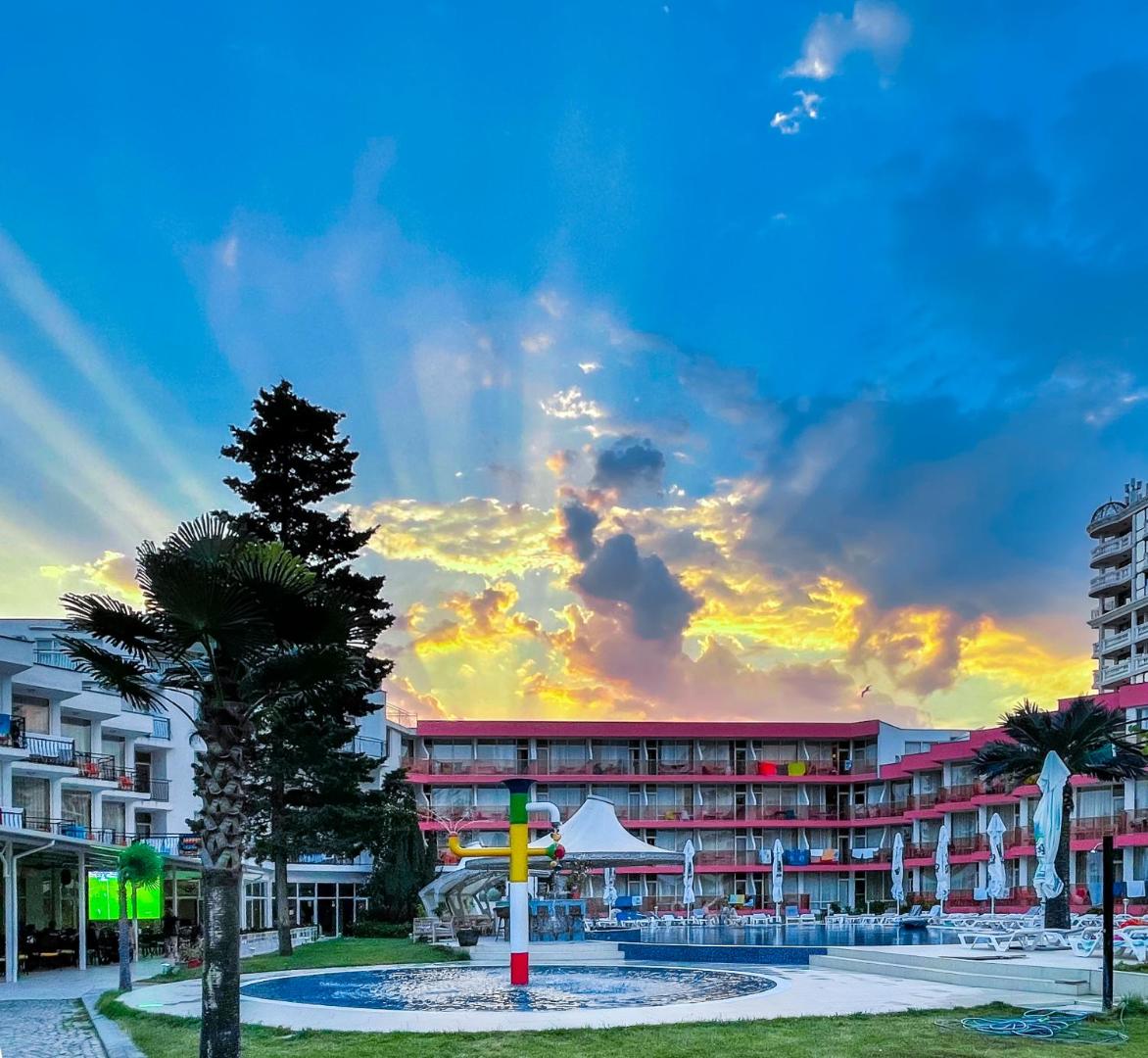 Flamingo Beach Hotel pagalms ar bērnu baseinu un strūklaku saulrieta laikā Saulainajā Krastā, Bulgārijā — debesis ar saules stariem