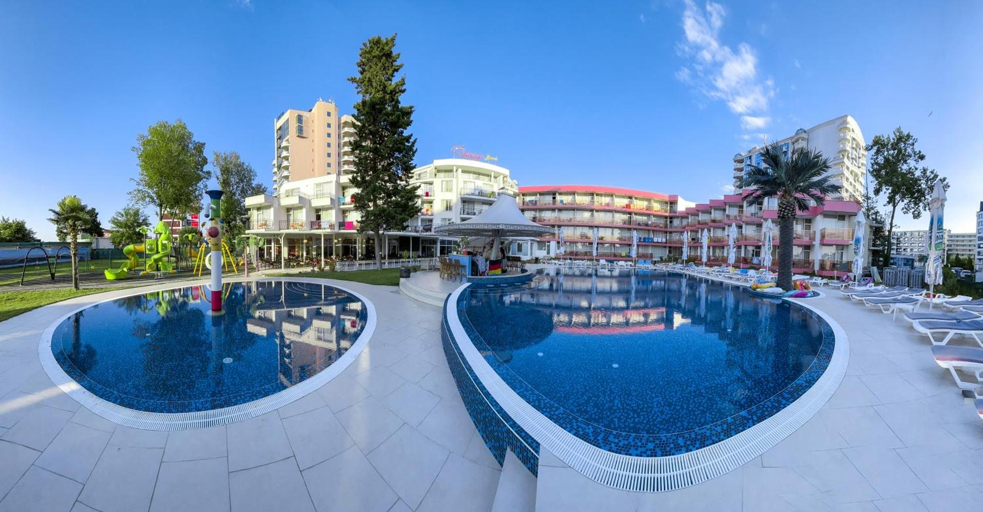 Flamingo Beach Hotel panorāmas skats uz āra baseinu kompleksu, bērnu rotaļu laukumu un viesnīcas korpusiem Saulainajā krastā