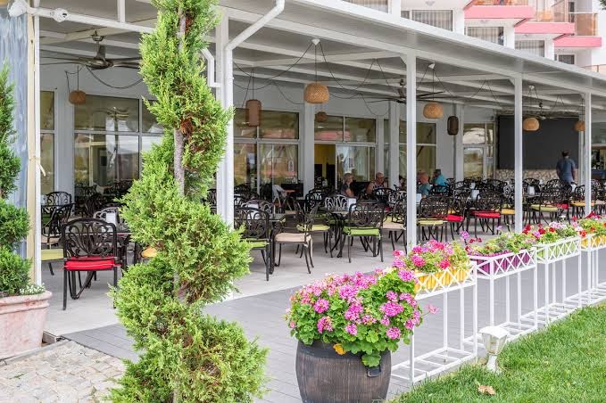Flamingo Beach Hotel āra terase ar galdiņiem, krēsliem un ziedu dekorācijām — mājīga atpūtas zona viesnīcas teritorijā