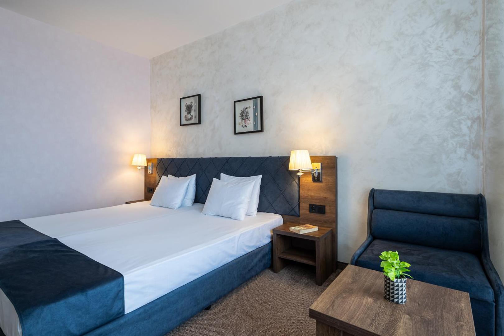 Flamingo Beach Hotel numura interjers ar divguļamo gultu, atpūtas krēslu un kafijas galdiņu gaišos un zilos toņos