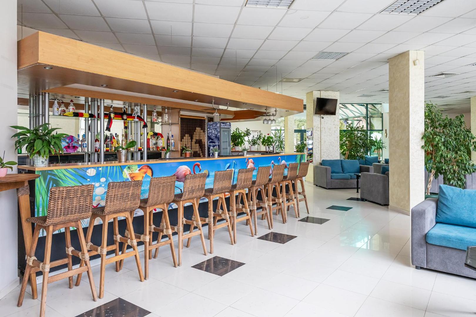 Flamingo Beach Hotel bārs ar tropisku dizainu, pītiem krēsliem un ziliem dīvāniem — plaša dzērienu izvēle un atpūtas zona