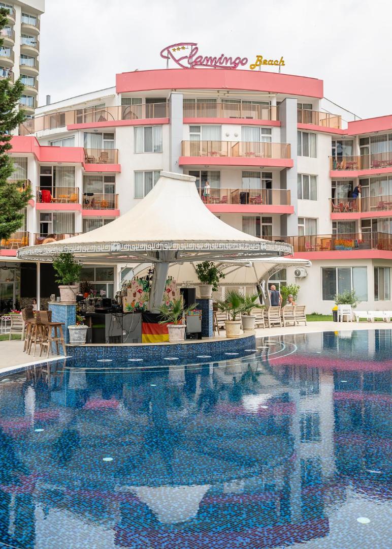 Flamingo Beach Hotel galvenā ēka ar baseinu un bāru zem nojumes Saulainajā Krastā — skats uz numuru balkoniem un atpūtas zonu