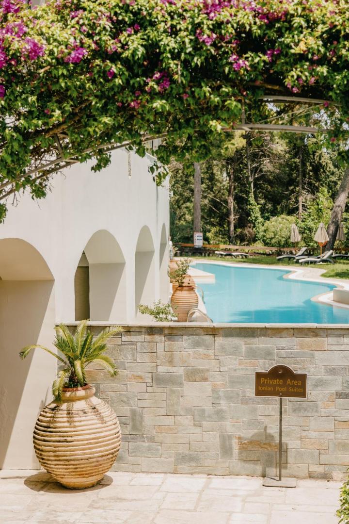 Corfu Holiday Palace Ionian Pool Suites privātā zona ar baseinu, ziedošiem augiem un tradicionālām grieķu amforām Korfu salā