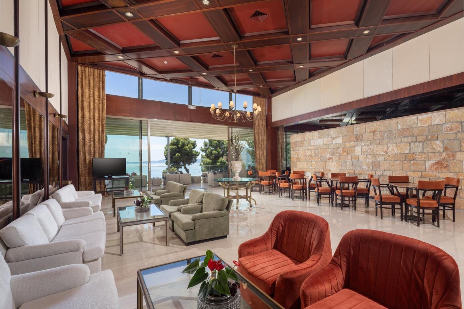 Corfu Holiday Palace lobby bārs ar klasisku koka griestu apdari, ērtiem dīvāniem un skatu uz dārzu Kanoni, Korfu