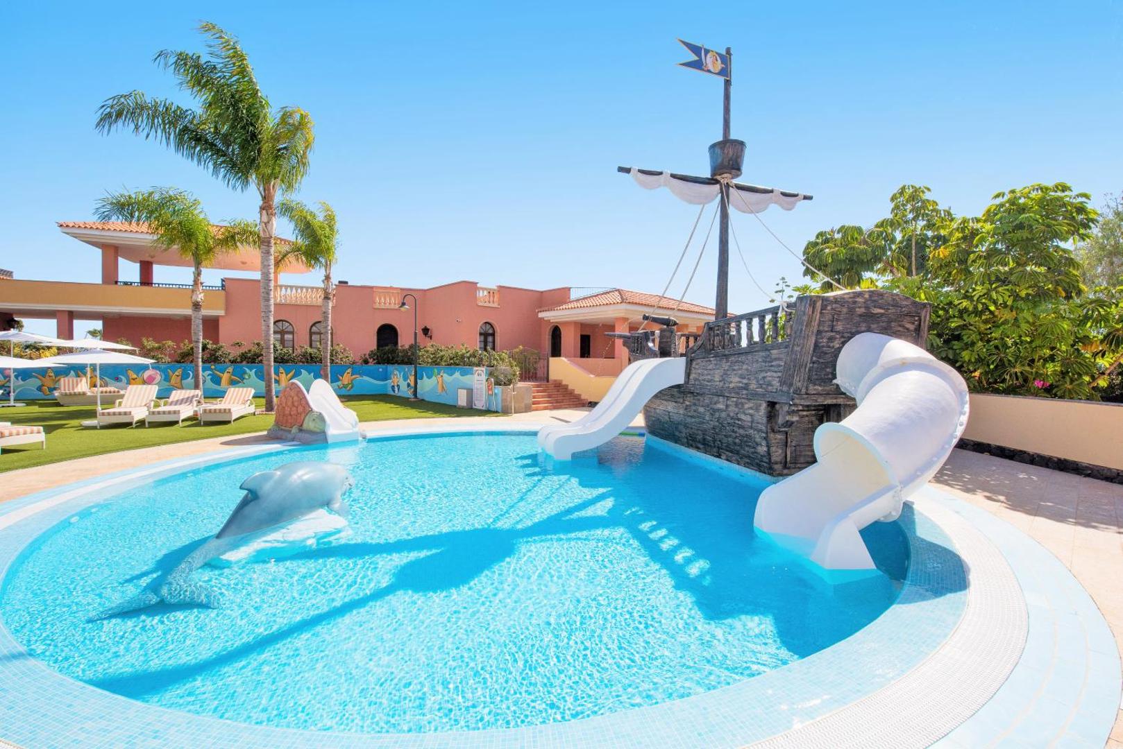 Iberostar Selection Anthelia bērnu baseins Tenerifē ar pirātu kuģi, slidkalniņiem un delfīna skulptūru saulainā dienā pie palmām