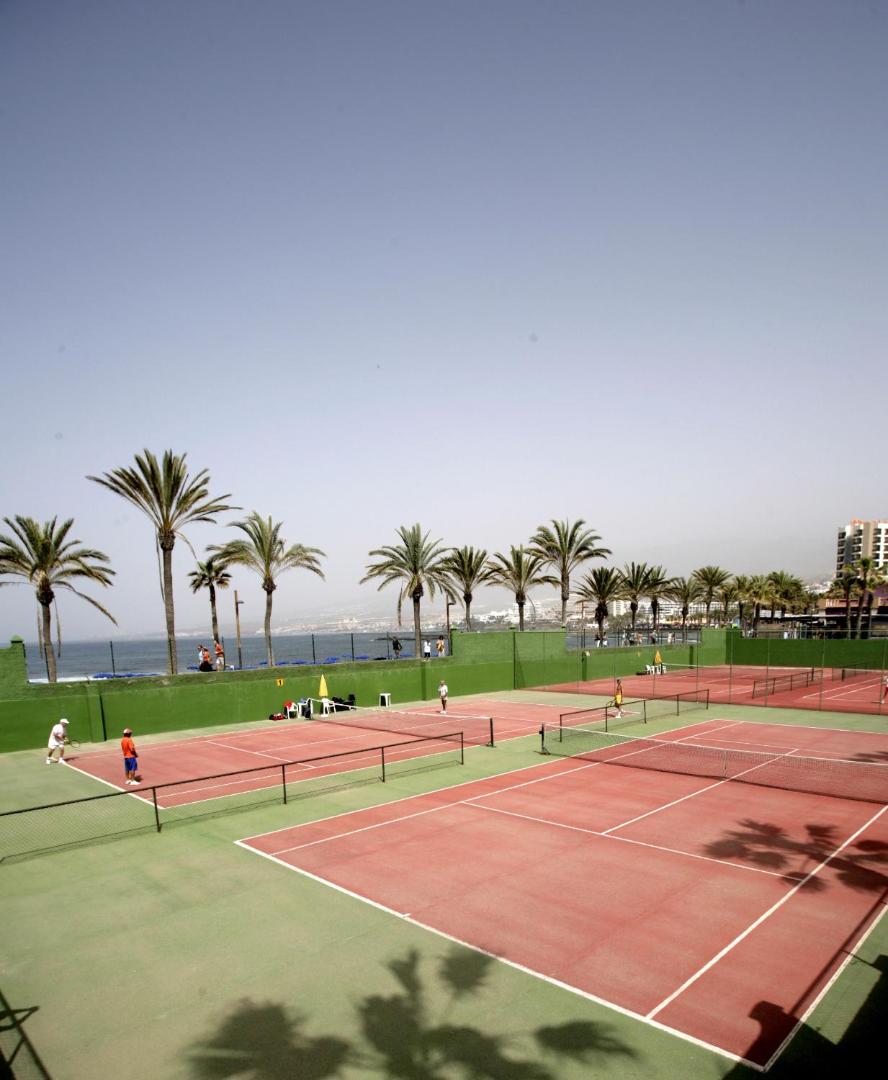 H10 Las Palmeras tenisa korti piekrastē ar skatu uz okeānu un palmām saulainā dienā Tenerifē