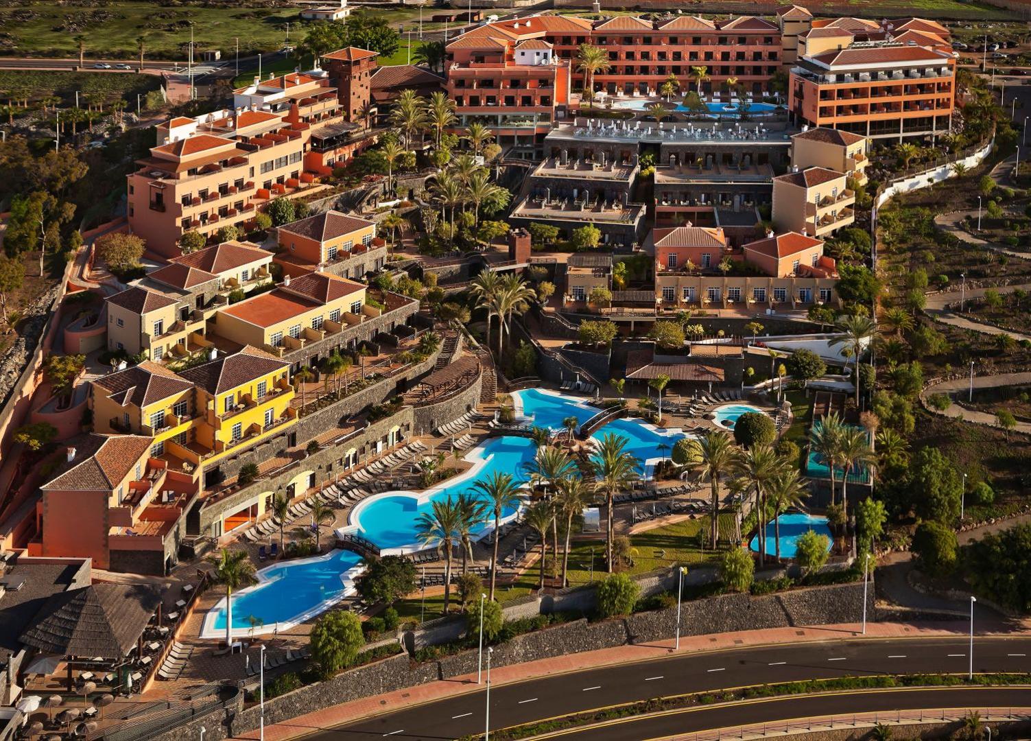 Meliá Jardines del Teide viesnīcas panorāmas skats Tenerifē ar vairākiem āra baseiniem, terasēm un palmu dārzu saulrieta gaismā