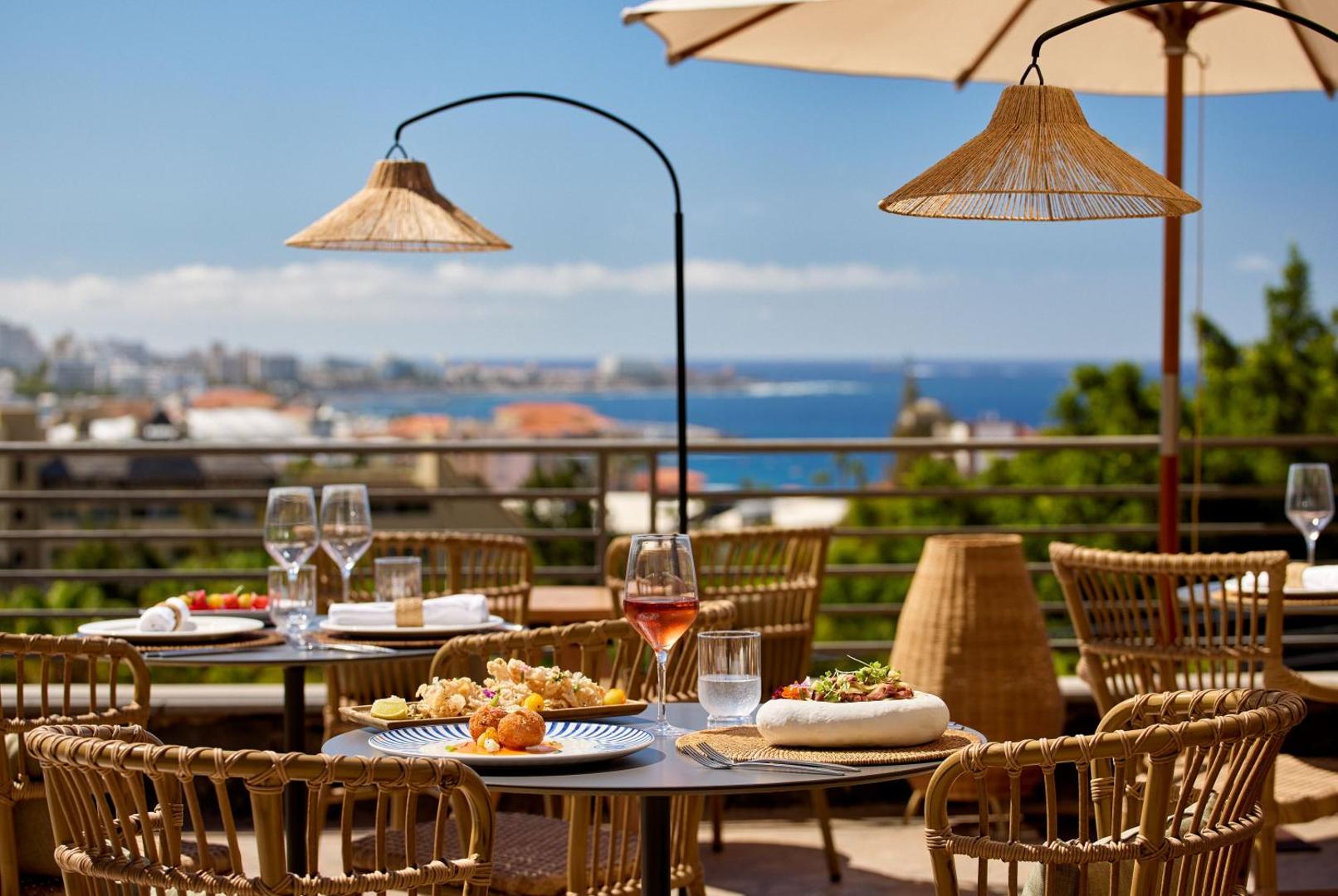 Restorāna galds uz Melia Jardines del Teide terases ar servētiem ēdieniem un vīnu, fonā okeāna panorāma