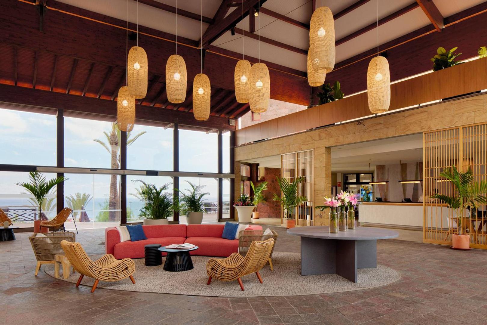 Viesnīcas Melia Jardines del Teide plašais lobby ar augstiem griestiem, stilīgām lampām un atpūtas zonu Tenerifes dienvidos