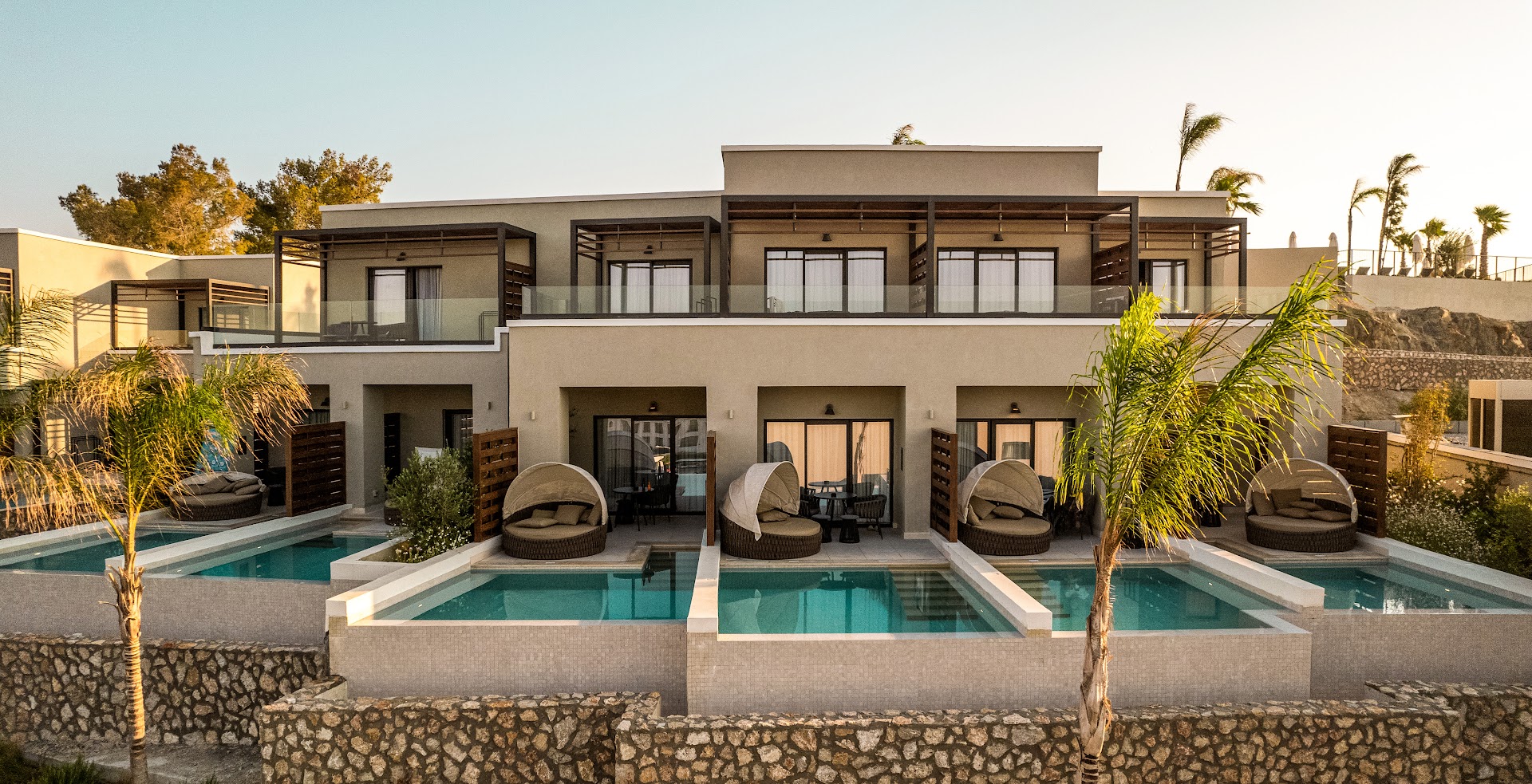 Mitsis Rodos Village viesnīcas korpuss Rodas salā ar privātiem baseiniem un atpūtas krēsliem pie katra numura saulrietā