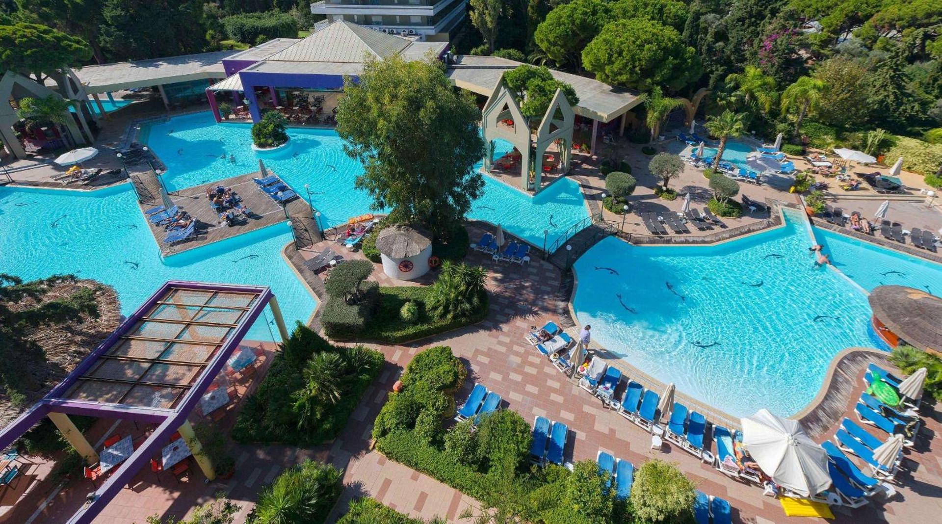 Dionysos viesnīcas plašais āra baseinu komplekss Rodas salā no putna lidojuma — tiltiņi, atpūtas krēsli un lekni dārzi