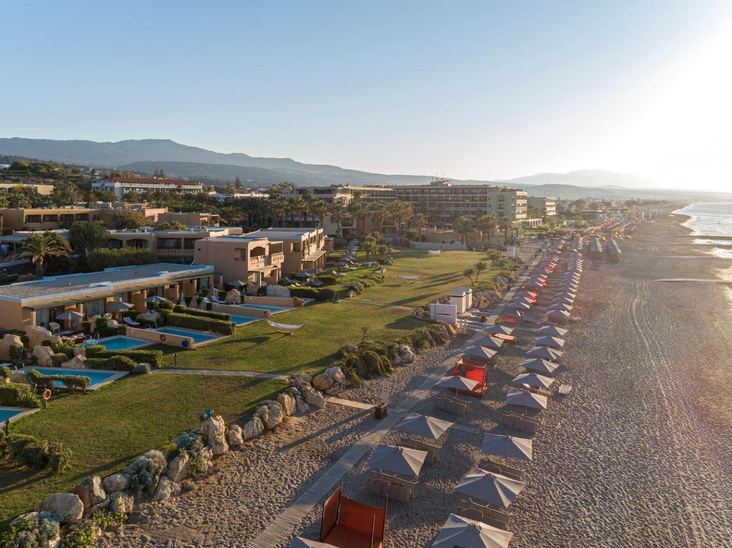 Skats no augšas uz Aquila Rithymna Beach pludmales zonu un bungalo tipa numuriem ar privātiem baseiniem saulrieta gaismā