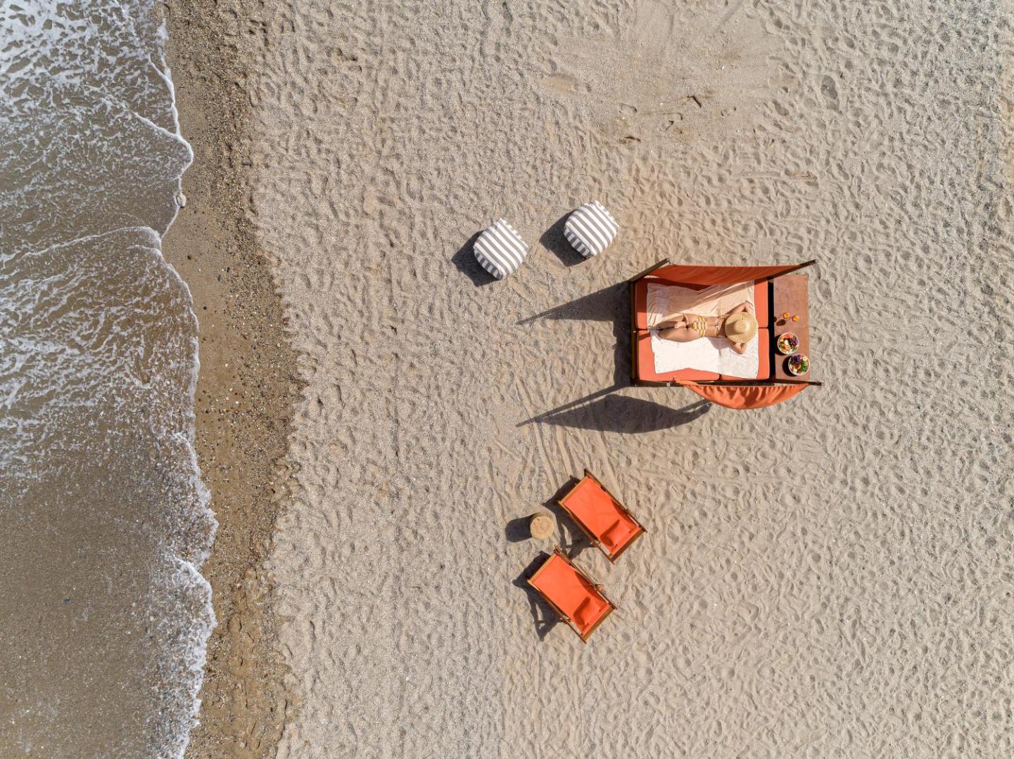 Aerofoto uzņēmums Aquila Rithymna Beach pludmalē, kur atpūtnieks bauda sauli uz oranža pludmales gultas pie pašas jūras malas Krētas piekrastē.