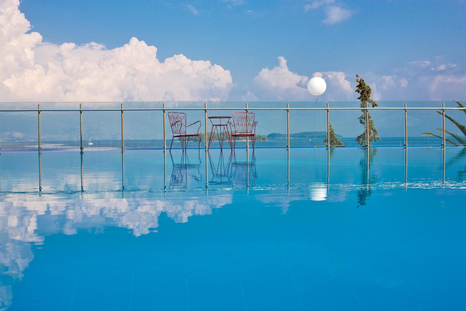 Kontokali Bay Resort & Spa bezmalas baseins ar dekoratīviem krēsliem un skatu uz jūru un kalniem tālumā