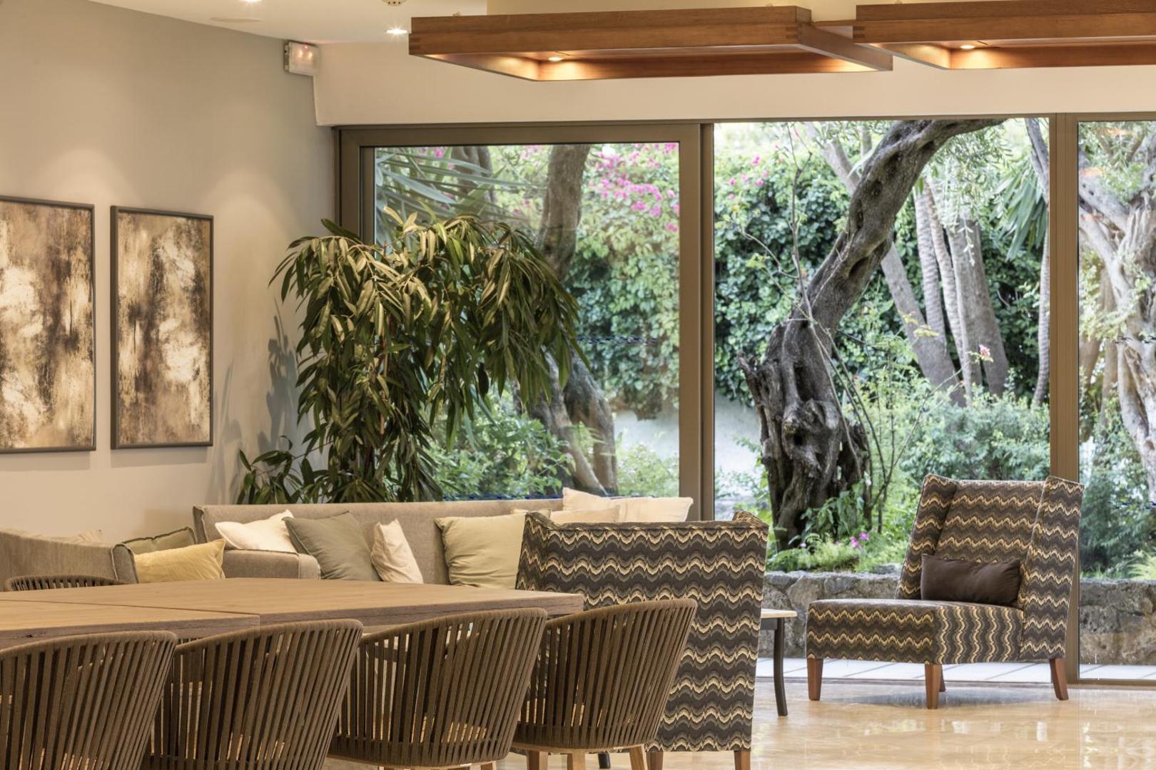 Kontokali Bay Resort & Spa lobby atpūtas telpa ar stilīgiem krēsliem un lieliem logiem, pa kuriem redzams dārzs