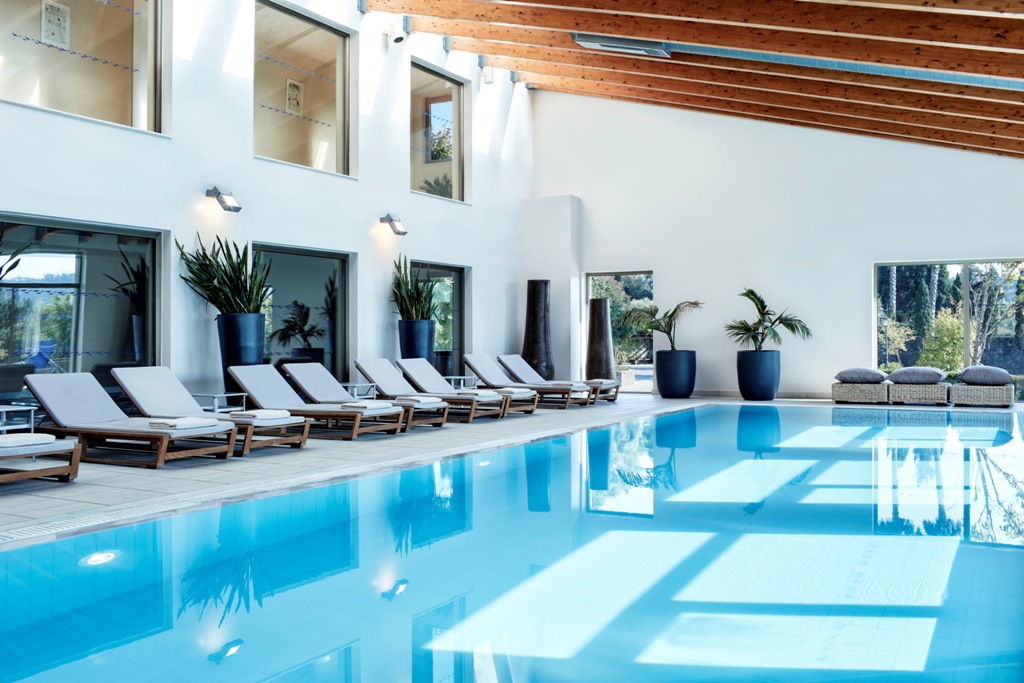Kontokali Bay Resort & Spa iekštelpu baseins ar panorāmas logiem, koka siju griestiem un ērtiem zviļņiem relaksācijai Grieķijā