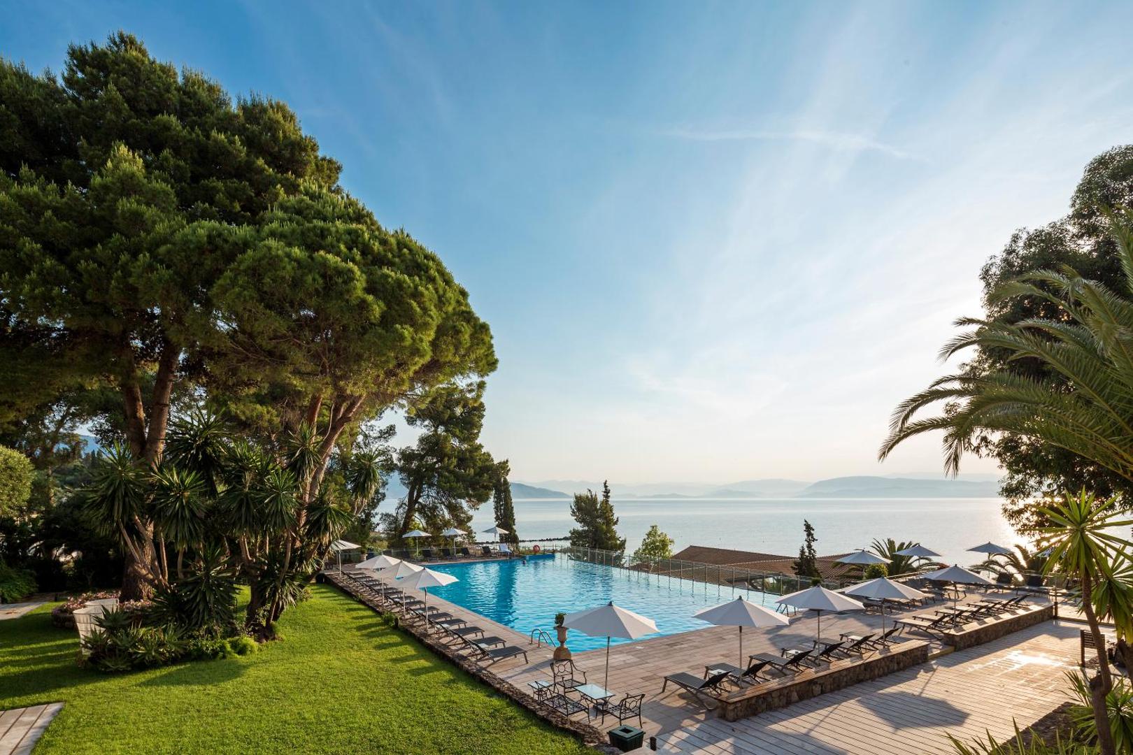 Kontokali Bay Resort & Spa āra baseins ar skatu uz Jonijas jūru Korfu salā, ko ieskauj zaļš dārzs un priedes