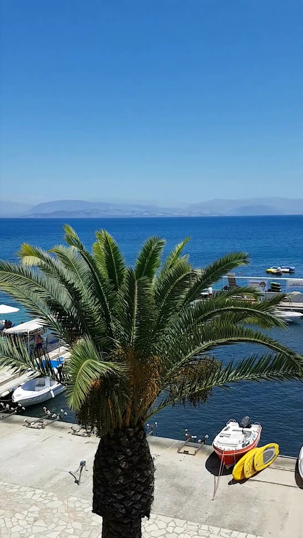 Kontokali Bay Resort & Spa laivu piestātne ar palmām un krāsainām laivām zilā Jonijas jūras fonā Korfu salā