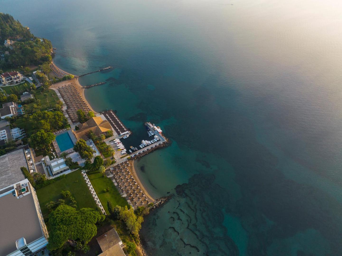 Kontokali Bay Resort & Spa piekrastes līnija saulrietā ar saulessargiem, baseinu un dzidru jūras ūdeni no augšas