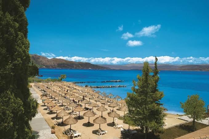 Kontokali Bay Resort & Spa pludmales zona no augšas, rādot smilšu krastu, daudzos saulessargus un zilo jūras līci Korfu