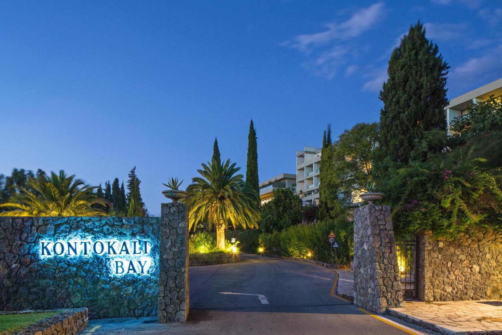 Kontokali Bay Resort & Spa izgaismota iebrauktuve un akmens mūris ar viesnīcas nosaukumu vakara stundā