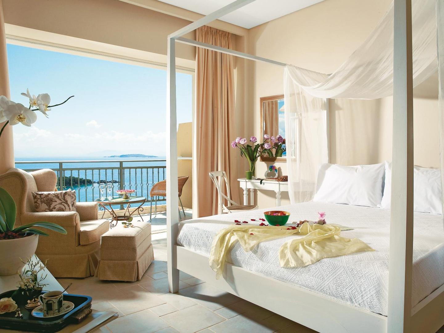 Grecotel Eva Palace gaišs numurs ar baldahīna gultu un skatu uz Jonijas jūru Korfu salā — elegants interjers ar balkonu