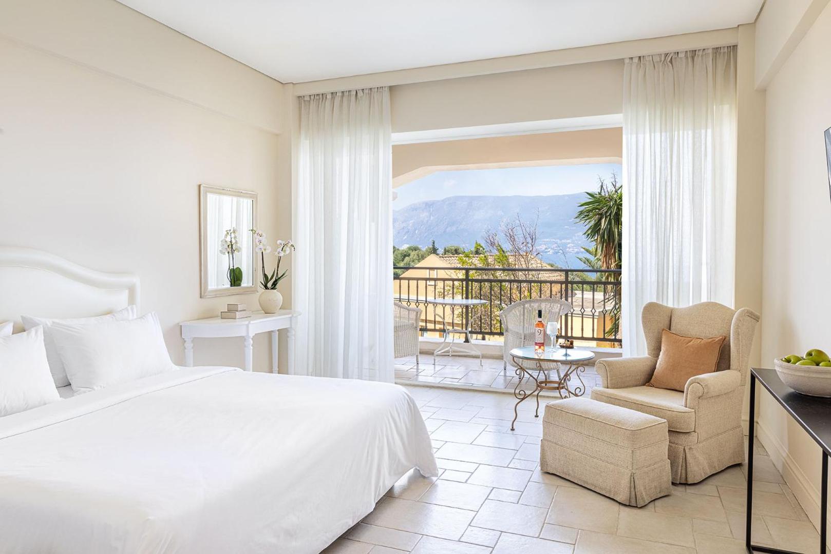 Grecotel Eva Palace gaišs numurs ar atpūtas zonu un skatu uz Korfu kalnaino ainavu no terases