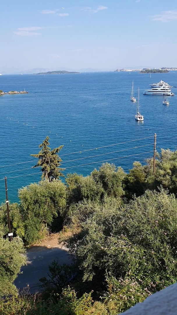 Grecotel Eva Palace skats no augšas uz Jonijas jūru Korfu piekrastē ar jahtām, buru laivām un zaļojošiem olīvkokiem