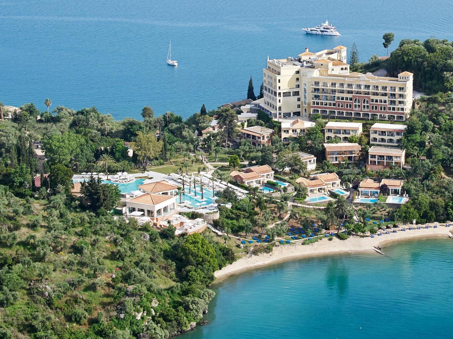 Grecotel Eva Palace galvenā ēka un bungalo komplekss piekrastē Korfu salā — redzams baseins, pludmales josla un jahtas jūrā.
