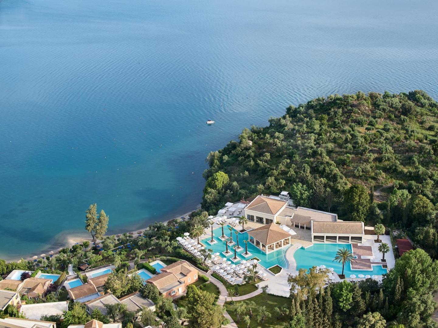 Grecotel Eva Palace plašais āra baseinu komplekss ar atpūtas zonām un palmām piekrastē, skats uz Jonijas jūru Korfu.