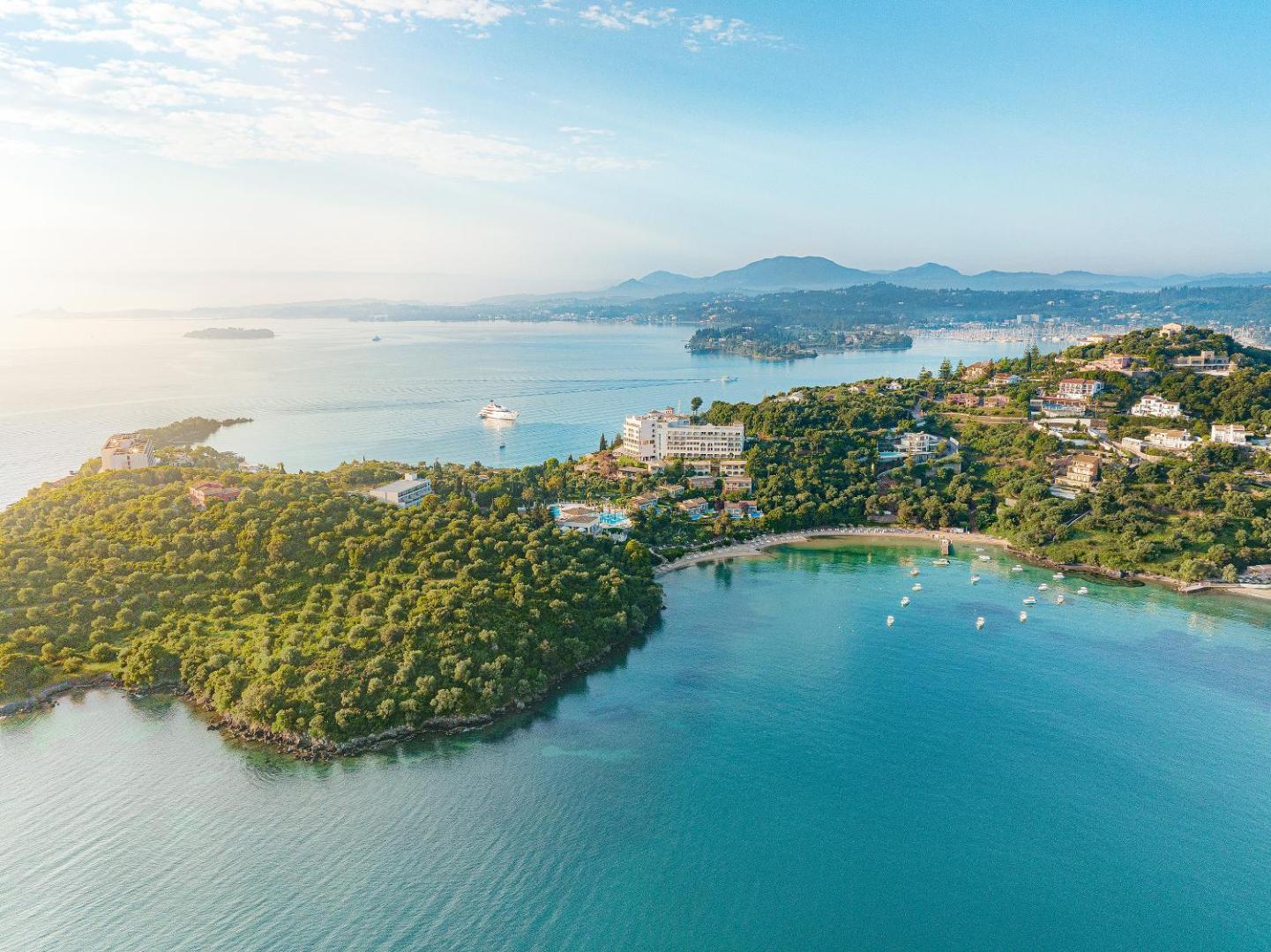 Grecotel Eva Palace viesnīcas panorāmas skats no putna lidojuma Kommeno pussalā, Korfu — apkārtnē tirkīzzila jūra, zaļojoši meži un privātie līči.