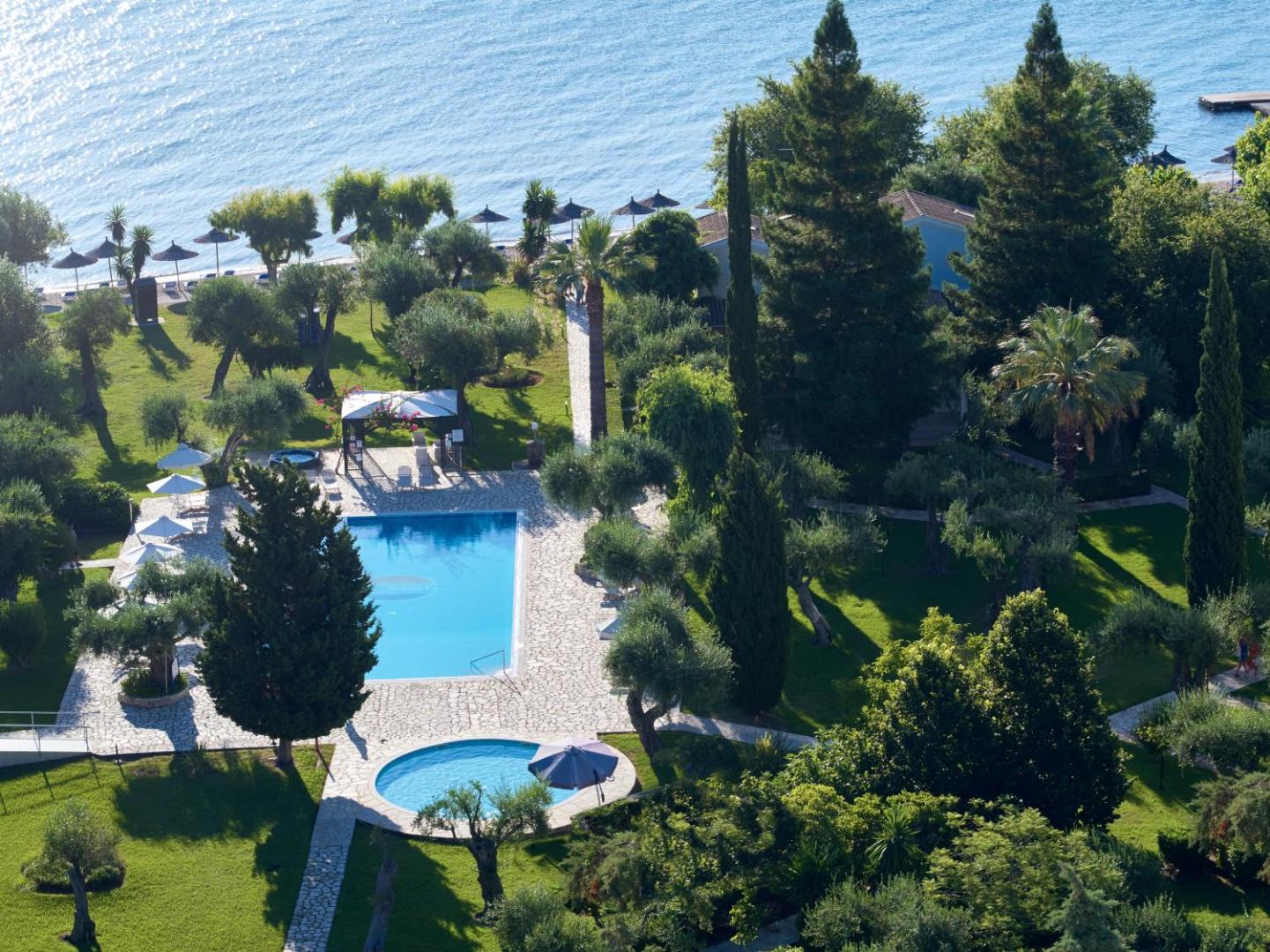 Delfinia Hotel skats no augšas uz āra baseinu un dārzu Korfu salā — apkārtnē zaļojoši koki un tieša piekļuve jūras krastam