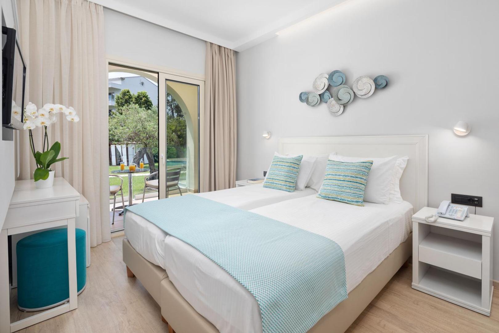Delfinia Hotel gaišs divvietīgs numurs ar balkonu un skatu uz dārzu — moderna apdare, balta gulta un zili akcenti
