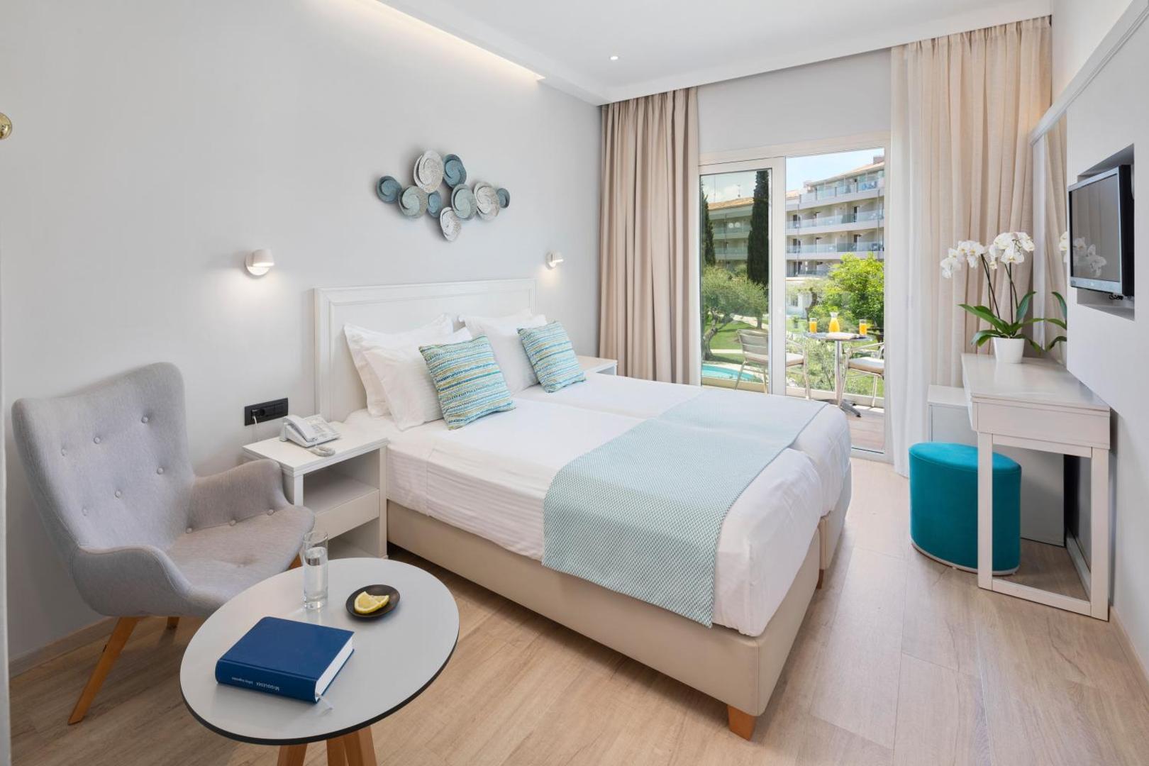 Delfinia Hotel moderns numurs ar atpūtas krēslu un skatu uz viesnīcas teritoriju un baseinu caur stikla durvīm