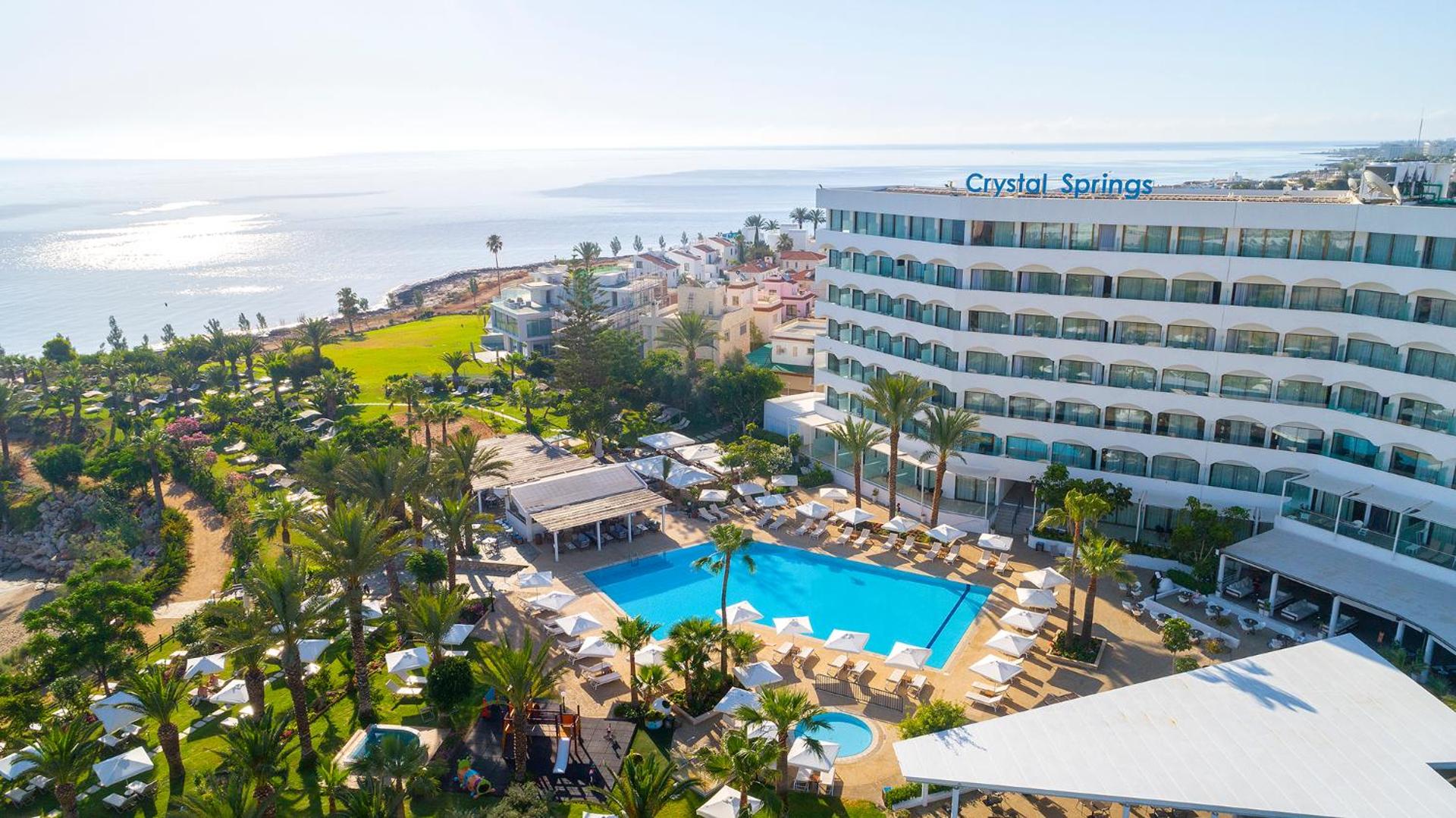 Crystal Springs Beach Hotel panorāmas skats Protarasā, Kiprā — galvenā ēka, āra baseins un dārzs Vidusjūras krastā saulainā dienā