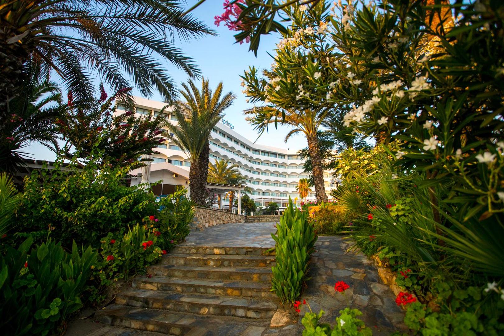 Crystal Springs Beach Hotel ieeja caur ziedošu dārzu un palmām — akmens pakāpieni ved uz viesnīcas galveno korpusu