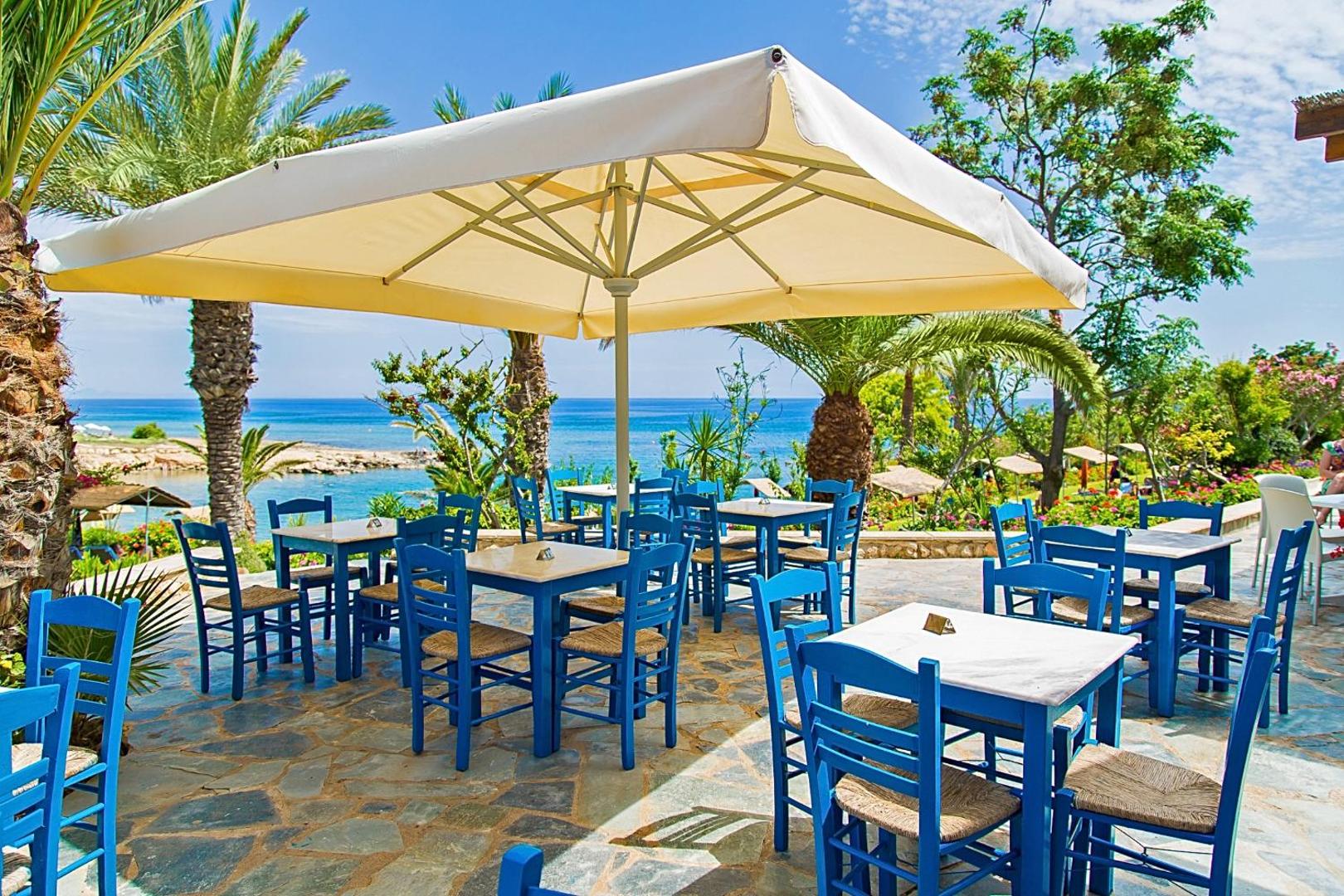 Grieķu stila āra restorāns Crystal Springs Beach viesnīcā ar ziliem koka krēsliem un skatu uz jūru