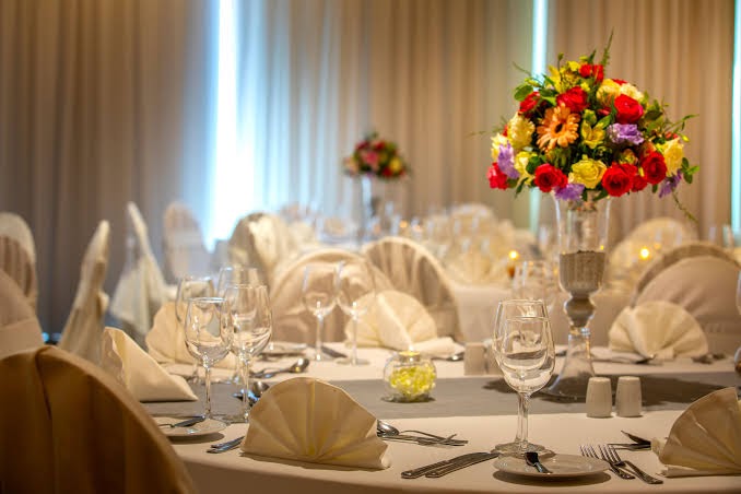 Svinīgi klāts galds Faros Hotel restorānā ar ziedu kompozīcijām un elegantiem traukiem banketu zālē