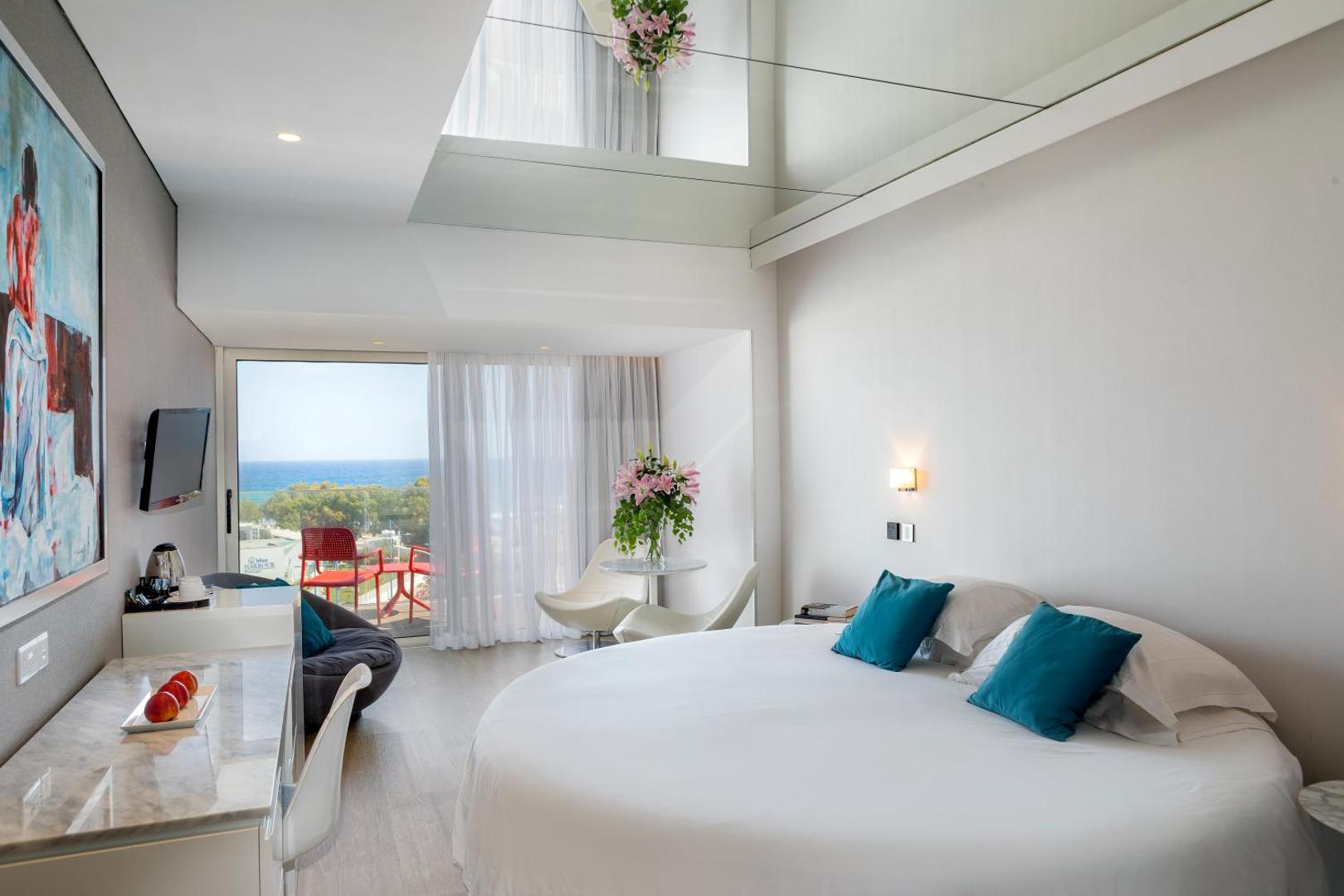Faros Hotel moderns numurs ar apaļu gultu, spoguļgriestiem un balkonu, no kura paveras skats uz Vidusjūru Kiprā