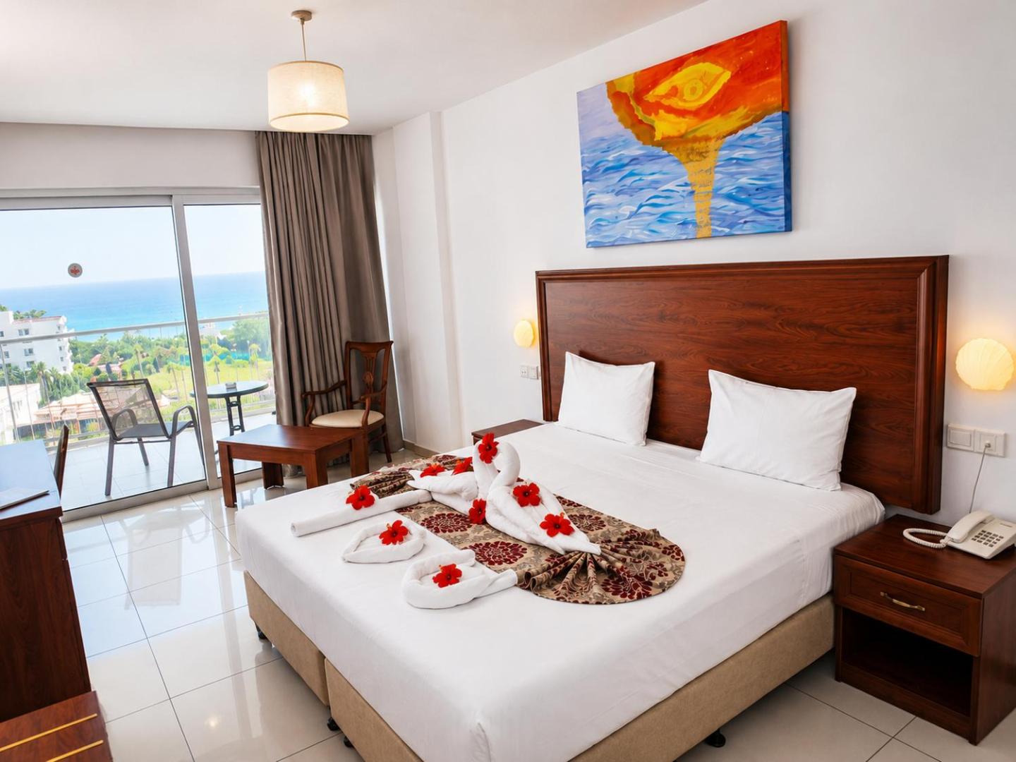 Viesnīcas Corfu Hotel numurs ar svētku noformējumu — dvieļu gulbji un ziedi uz gultas, skats uz piekrasti