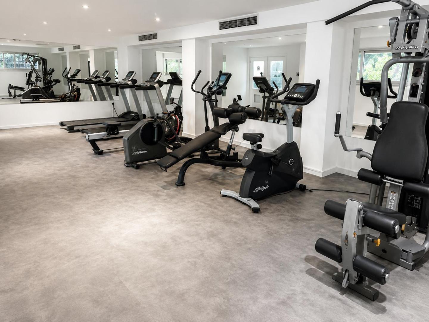 Corfu Hotel moderns fitness centrs ar LifeFitness trenažieriem, skrejceļiem un velotrenažieriem gaišā telpā ar spoguļiem