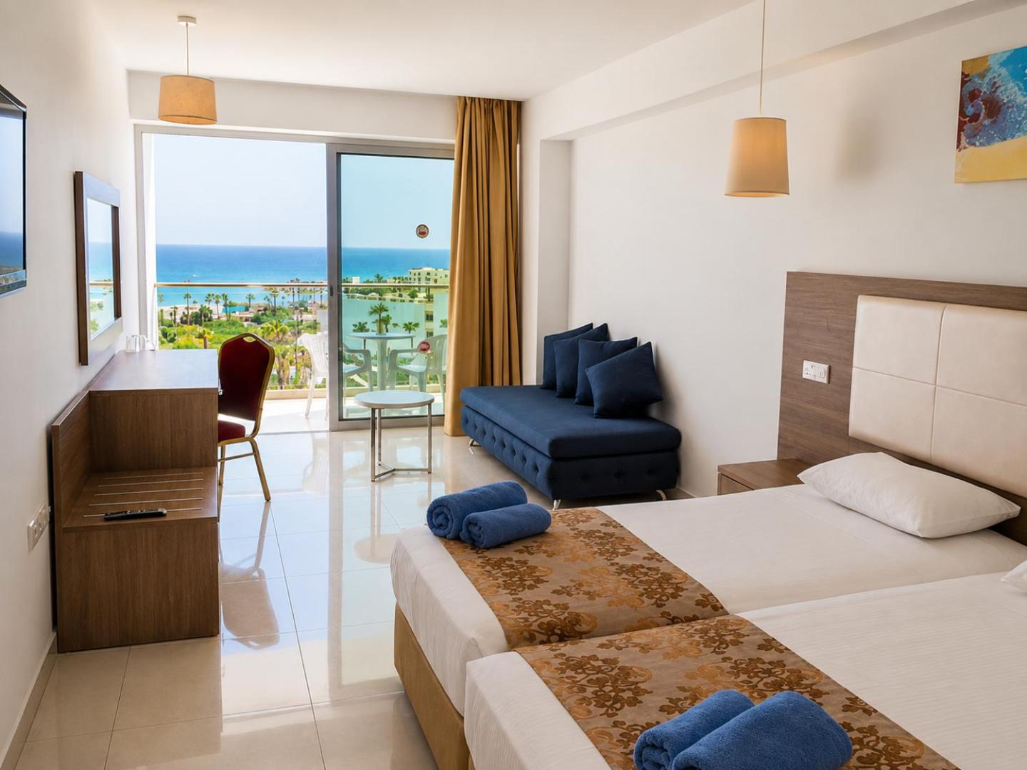 Corfu Hotel gaišs divvietīgs numurs ar balkonu un skatu uz Vidusjūru Aijanapā, Kiprā — zils dīvāns un rakstāmgalds