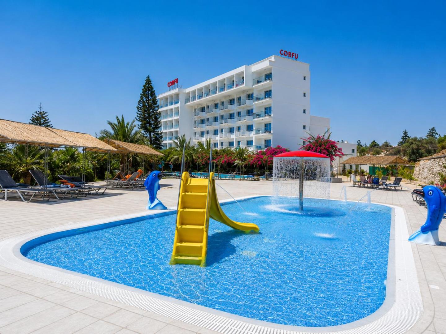 Corfu Hotel galvenā ēka un bērnu baseins ar dzeltenu slidkalniņu, strūklakām un delfīnu figūrām Ajanapā