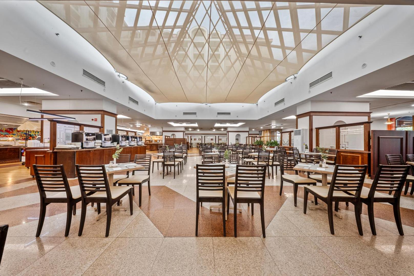 Melia Grand Hermitage viesnīcas plašā restorāna zāle ar koka apdari un stikla griestu konstrukciju Zelta Smiltīs, Bulgārijā
