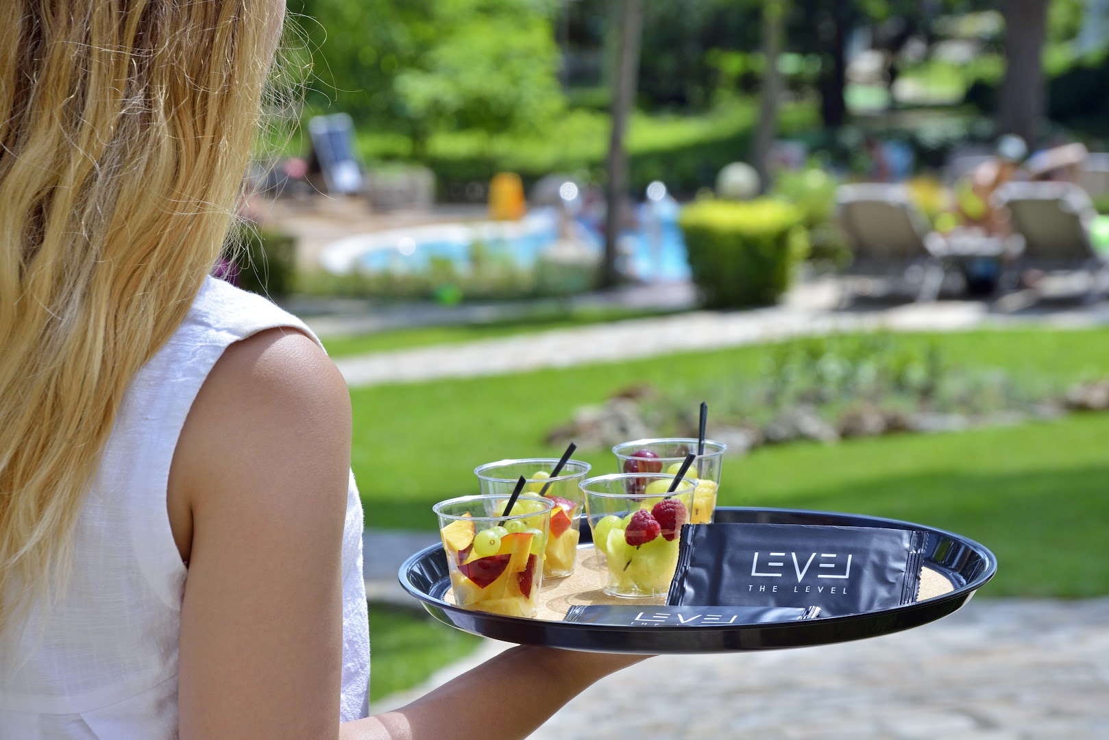 Viesnīcas darbinieks pasniedz svaigu augļu uzkodas The Level zonā Melia Grand Hermitage dārzā pie baseina