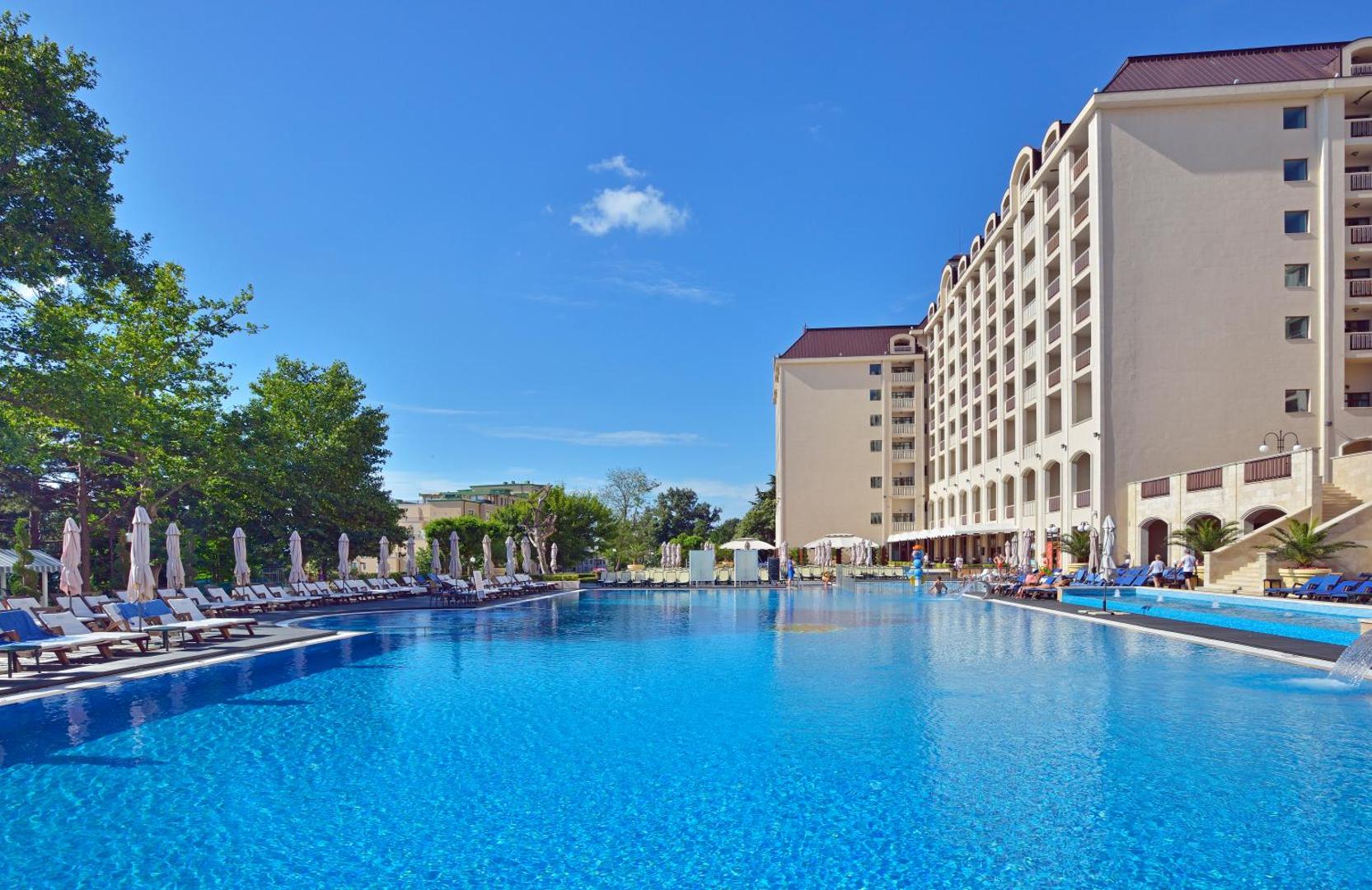 Melia Grand Hermitage lielais āra baseins Zelta Smiltīs, Bulgārijā — plaša sauļošanās zona ar atpūtas krēsliem pie viesnīcas galvenās ēkas