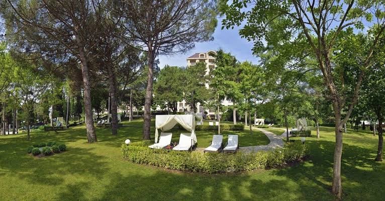 Melia Grand Hermitage plašā dārza teritorija ar atpūtas krēsliem zem priedēm un skatu uz viesnīcas ēku