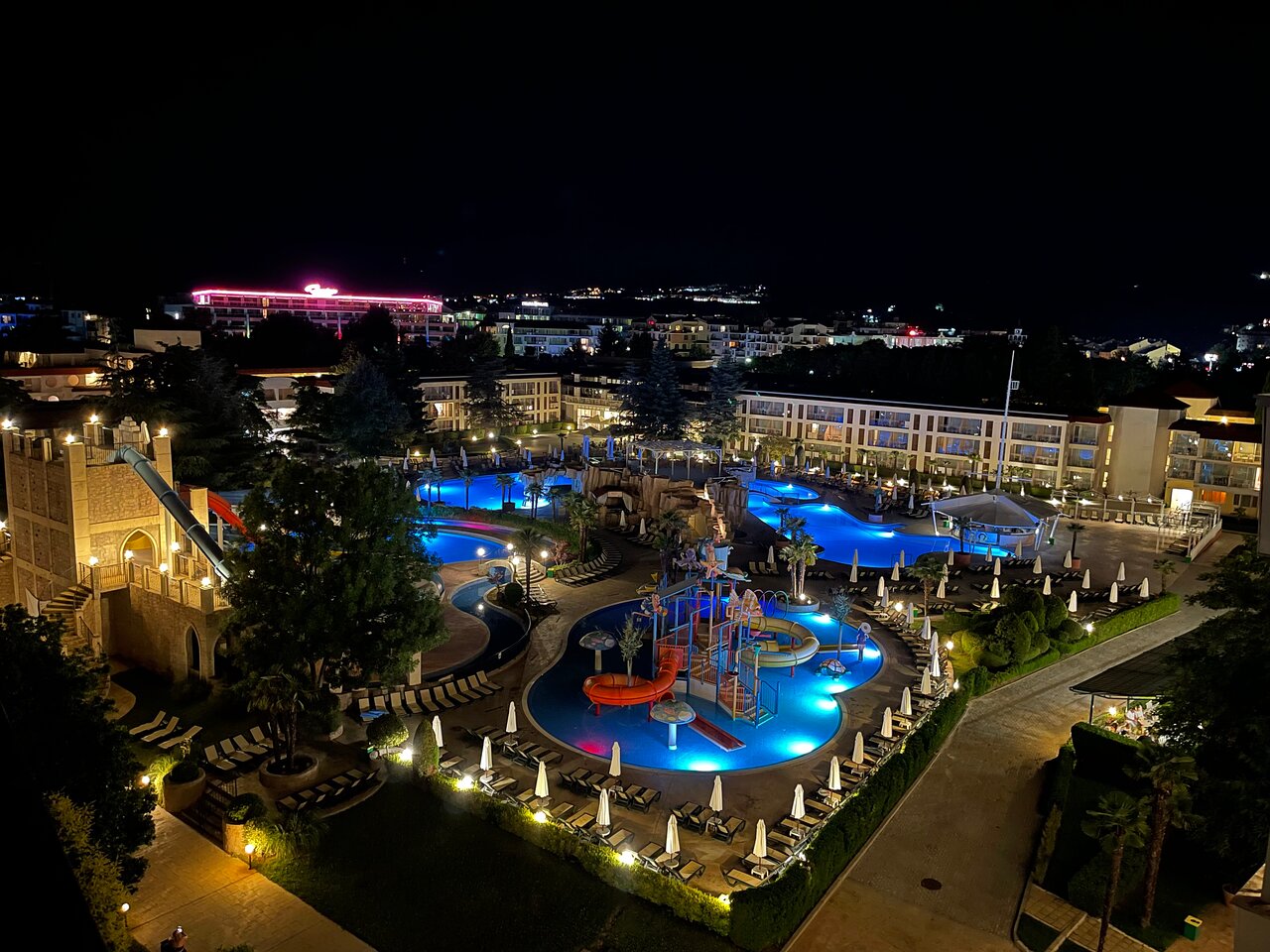 DIT Evrika Beach Club Hotel akvaparks un baseini naktī — izgaismotas ūdens atrakcijas un viesnīcas teritorija Saulainajā krastā